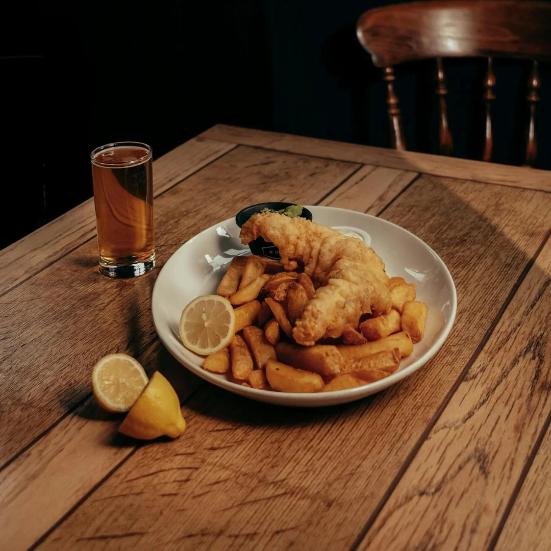 A golden, crispy battered fish served with thick-cut chips, garnished with a lemon wedge and fresh parsley, on a plate at one of Worthing's best fish and chip shops