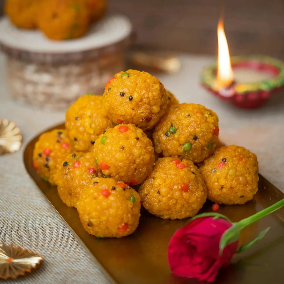 A plate filled with golden-brown Indian laddoos, traditional sweet round balls made from flour, sugar, and ghee, garnished with nuts and perfect for festive occasions