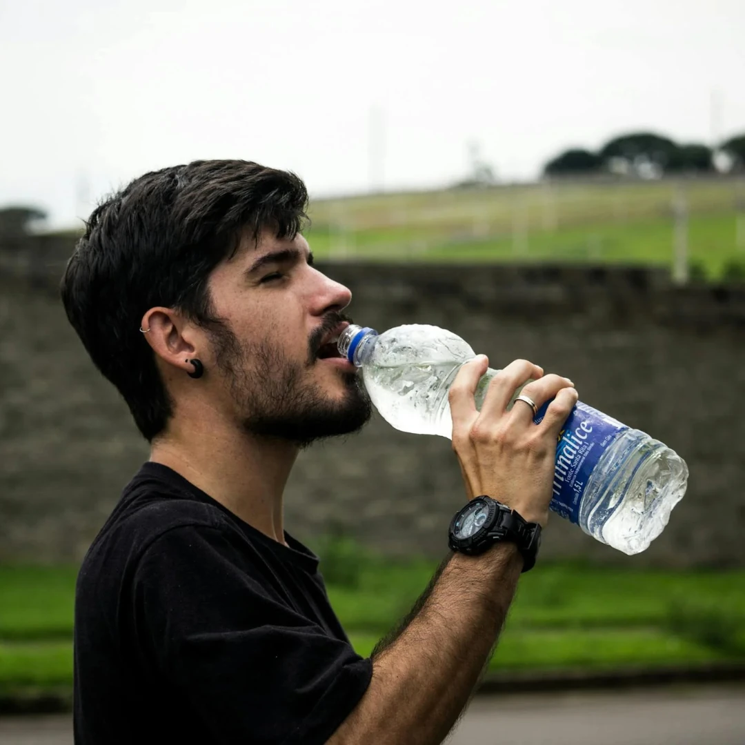 A person drinking from a plastic water bottle outdoors, with a focus on hydration and a natural, relaxed setting.